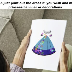 May include: A printable paper craft of a blue princess dress with colorful floral and butterfly designs. The dress is shown on a white sheet of paper held by a person's hands.