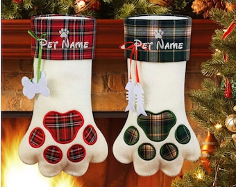 May include: Two Christmas stockings shaped like a paw, with a white base and plaid accents. The top band reads "PET NAME" and features a paw print. One has a bone, the other has fish. Festive holiday decor.