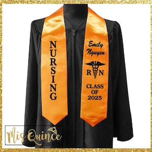 May include: Black graduation gown with an orange nursing sash. The sash has the word "NURSING" vertically printed on one side and the name "Emily Nguyen", the Registered Nurse symbol, and "CLASS OF 2025" on the other.
