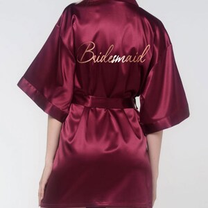 May include: A burgundy satin robe with the word 'bridesmaid' embroidered on the back in gold lettering.