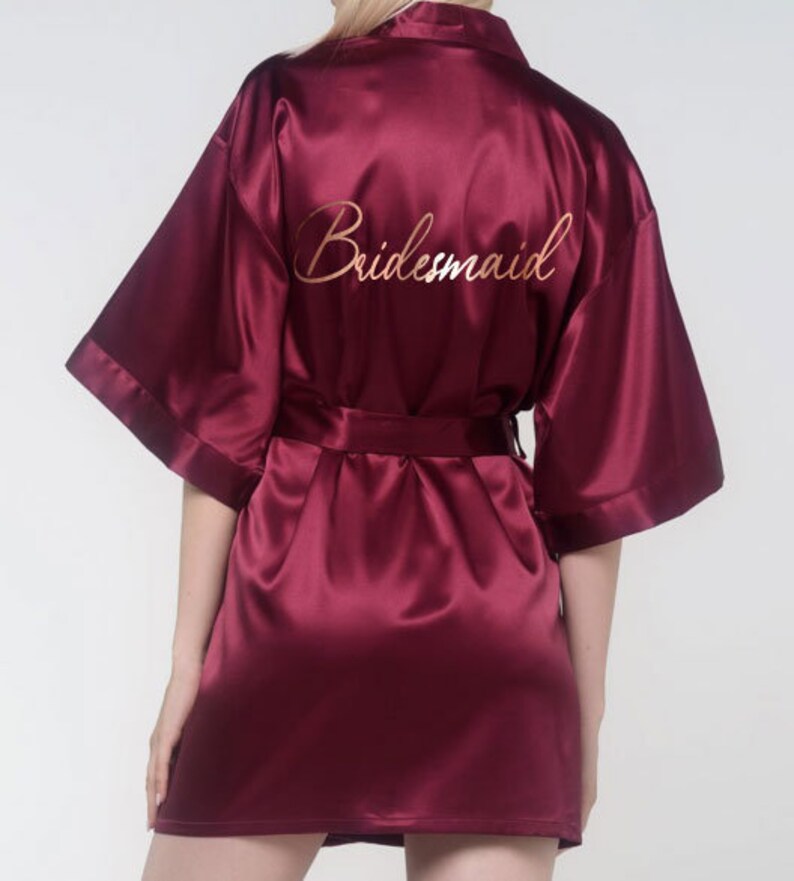 May include: A burgundy satin robe with the word 'bridesmaid' embroidered on the back in gold lettering.