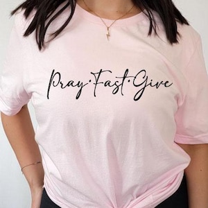 May include: A pink t-shirt with the text "Pray. Fast. Give" printed in black.
