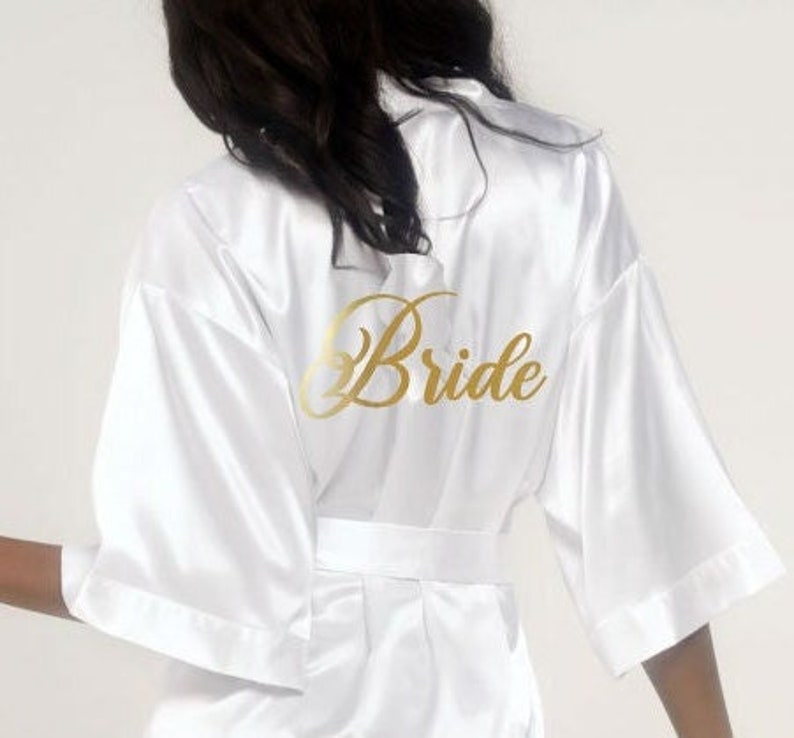 May include: A white satin robe with gold lettering that says 'Bride' on the back.