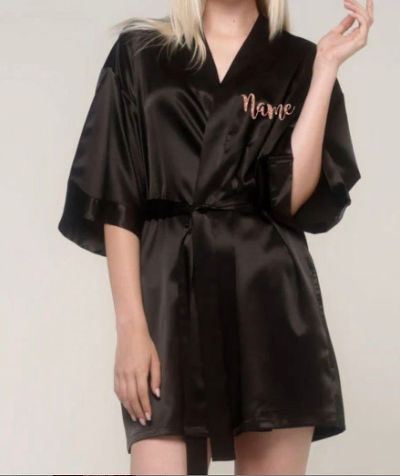May include: A black satin robe with a rose gold embroidered name on the left side of the chest.