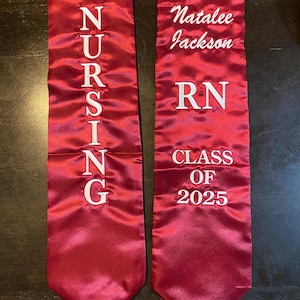 May include: Two maroon graduation stoles. One stole reads "NURSING" in white lettering. The other stole reads "Natalee Jackson", "RN", and "CLASS OF 2025" in white lettering.