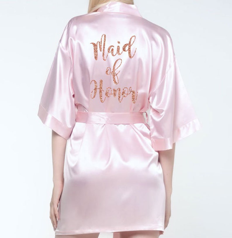 May include: A pink satin robe with the words 'Maid of Honor' in gold glitter lettering on the back.
