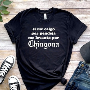 May include: Black t-shirt with white text that reads "si me caigo por pendeja me levanto por Chingona".