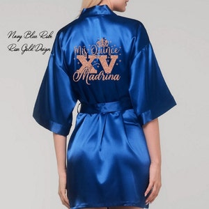 May include: Navy blue satin robe with a rose gold design that says "Miss Quince XV Madrina" on the back.