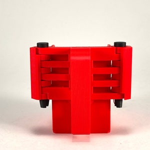 Puede incluir: Un objeto de pl&aacute;stico rojo con una serie de ranuras y botones negros en los lados. El objeto est&aacute; dise&ntilde;ado para contener varios art&iacute;culos.