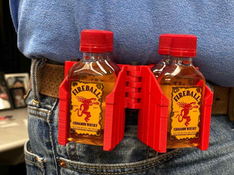 Puede incluir: Porta-botellas de pl&aacute;stico rojo para dos botellas peque&ntilde;as de whisky de canela Fireball. El porta-botellas est&aacute; sujeto a un cintur&oacute;n.