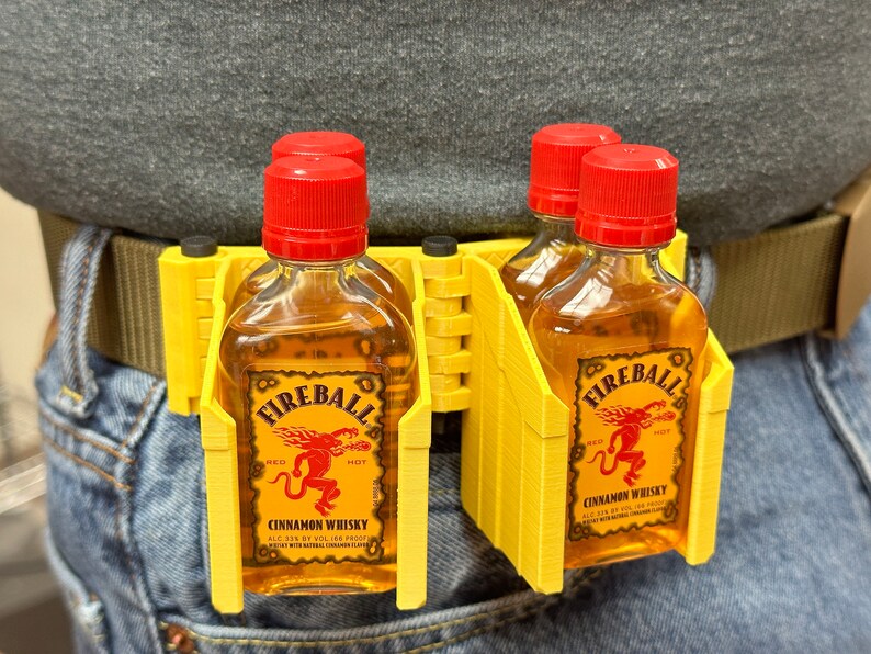 Puede incluir: Porta botellas de pl&aacute;stico amarillo para cuatro botellas peque&ntilde;as de whisky de canela Fireball. El porta botellas est&aacute; sujeto a un cintur&oacute;n marr&oacute;n y se lleva en la cintura.