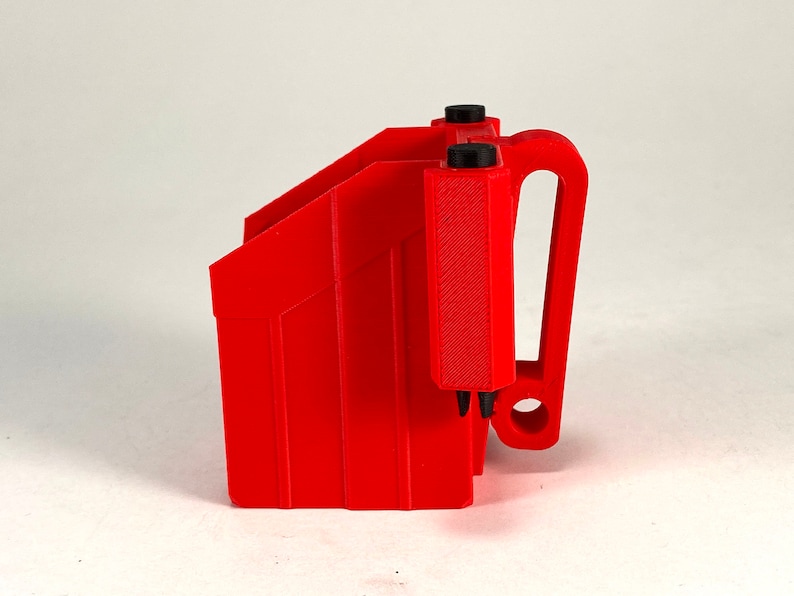 Puede incluir: Un portacargadores de pl&aacute;stico rojo con un clip para cintur&oacute;n. El portacargadores tiene una superficie texturizada y un asa negra.