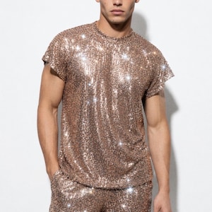 Könnte beinhalten: Ein roségoldenes Pailletten-T-Shirt und Shorts-Set. Das Oberteil hat einen Rundhalsausschnitt und kurze Ärmel, während die Shorts Taschen haben. Das Outfit ist so konzipiert, dass es das Licht einfängt und einen schillernden Effekt erzeugt.