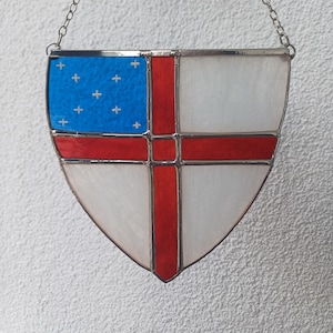 May include: A stained glass shield with a red cross on a white background. The top section of the shield is blue with white crosses.