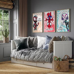 May include: Three framed superhero art prints with the text "I AM BRAVE", "I AM POLITE", and "I AM LOVED" hang above a white daybed with a patterned comforter and pillows. A woven basket with tassels sits on the floor.