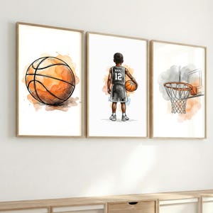 Könnte beinhalten: Set aus drei gerahmten Kunstdrucken zum Thema Basketball. Die Drucke zeigen einen Basketball, einen Basketballspieler mit der Nummer 12 und einen Basketballkorb. Die Kunstwerke haben einen Aquarell-Effekt mit Orange- und Brauntönen.