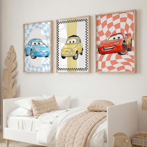 Pode incluir: Tr&ecirc;s impress&otilde;es de arte emolduradas com tema de carros. As impress&otilde;es apresentam carros de desenho animado em azul, amarelo e vermelho, em fundos quadriculados e ovais. As molduras s&atilde;o de cor de madeira clara e a obra de arte &eacute; exibida acima de uma cama branca.