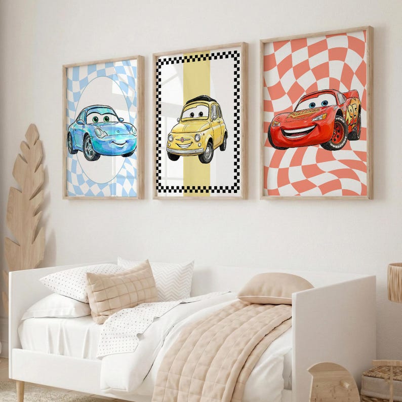 Pode incluir: Tr&ecirc;s impress&otilde;es de arte emolduradas com tema de carros. As impress&otilde;es apresentam carros de desenho animado em azul, amarelo e vermelho, em fundos quadriculados e ovais. As molduras s&atilde;o de cor de madeira clara e a obra de arte &eacute; exibida acima de uma cama branca.