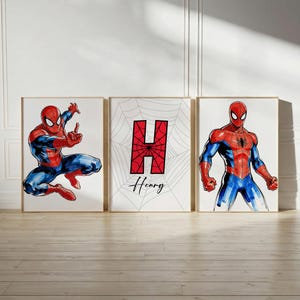 May include: Three framed art prints featuring Spider-Man illustrations. One shows Spider-Man in action, another displays a red "H" with "Henry" below, and the third depicts Spider-Man standing. The artwork is in red, blue, and black.