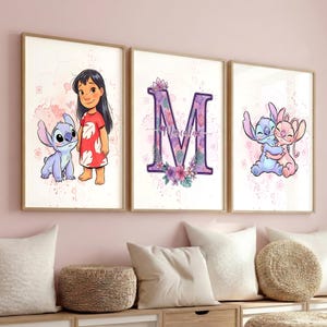 Puede incluir: Tres impresiones artísticas enmarcadas con personajes de dibujos animados. Una impresión muestra a una niña con un extraterrestre azul. Otra muestra la letra "M" con detalles florales y un nombre. La tercera representa a dos extraterrestes abrazándose. Las impresiones tienen un fondo rosa claro.