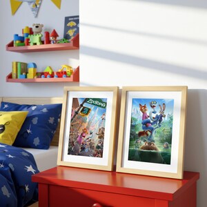 May include: Two framed Zootopia movie posters with light wood frames sit on a red table. The posters feature colorful illustrations of the animated characters. The background includes a bed with blue bedding and a shelf with toys.