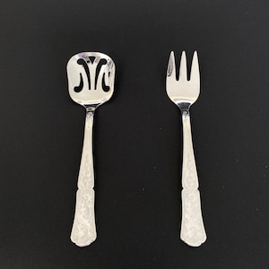 May include: A set of two silver-plated utensils, a fork and a spoon with an ornate design. The spoon has a decorative cutout in the bowl.