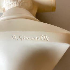 Op de afbeelding: Een cr&egrave;mekleurige borstbeeldsculptuur met gedetailleerde gelaatstrekken en haar. De sculptuur heeft een gladde afwerking en de naam "A. Giannelli" is op de basis gegraveerd. Het borstbeeld is een klassiek kunstwerk.