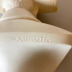Op de afbeelding: Een cr&egrave;mekleurige borstbeeldsculptuur met gedetailleerde gelaatstrekken en haar. De sculptuur heeft een gladde afwerking en de naam "A. Giannelli" is op de basis gegraveerd. Het borstbeeld is een klassiek kunstwerk.