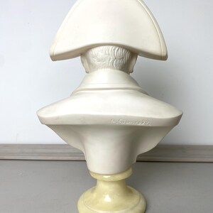 Op de afbeelding: Een cr&egrave;mekleurige buste van een historische figuur, van achteren bekeken. De sculptuur heeft een steek en een hoge kraag. De buste is gemonteerd op een lichtgele sokkel. De tekst "A. Giummelli" is zichtbaar.