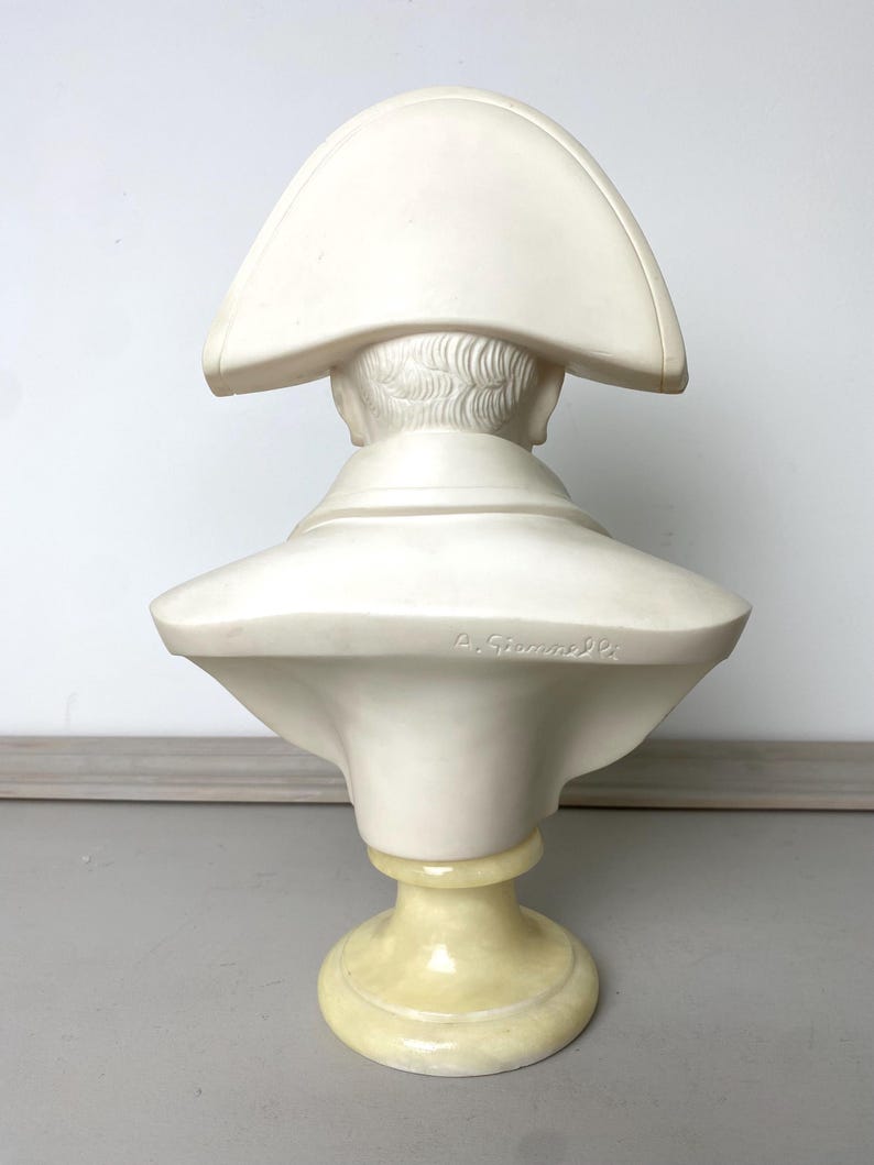 Op de afbeelding: Een cr&egrave;mekleurige buste van een historische figuur, van achteren bekeken. De sculptuur heeft een steek en een hoge kraag. De buste is gemonteerd op een lichtgele sokkel. De tekst "A. Giummelli" is zichtbaar.