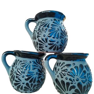 Puede incluir: Tres tazas de cer&aacute;mica azul con dise&ntilde;os florales negros. Las tazas tienen un cuerpo redondeado y una sola asa.