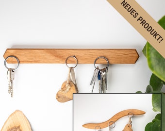 Può includere: Porta chiavi in legno con tre ganci e finitura in legno naturale. Il porta chiavi è montato su una parete bianca. Il testo "NEUES PRODUKT!" è visibile nell'angolo in alto a destra dell'immagine.