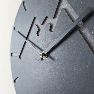 May include: A black clock with a unique mountain-shaped design. The clock has black hands and a gold centre.