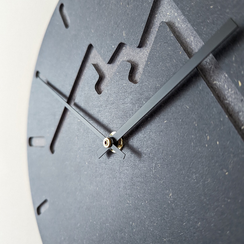 May include: A black clock with a unique mountain-shaped design. The clock has black hands and a gold centre.