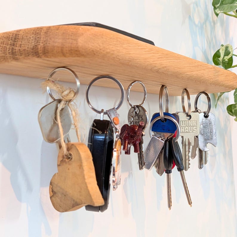 Op de afbeelding: Een houten sleutelhouder met een natuurlijke afwerking, met verschillende sleutels en sleutelhangers die aan metalen haken hangen. Inclusief een houten hartvormige sleutelhanger en een autosleutel.