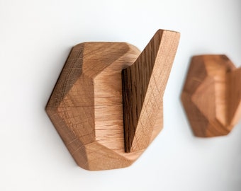 May include: Two wooden wall hooks in the shape of geometric shapes. The hooks are made of light brown wood and have a natural finish. The hooks are mounted on a white wall.