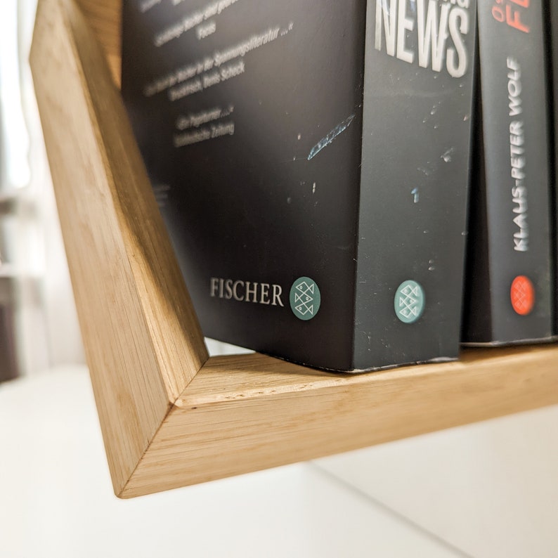 K&ouml;nnte beinhalten: Ein Holzregal mit drei B&uuml;chern darauf. Das Buch links hat einen schwarzen Einband mit dem Wort "FISCHER" und einem Logo. Das Buch in der Mitte hat einen schwarzen Einband mit dem Wort "NEWS" darauf. Das Buch rechts hat einen roten Einband mit den Worten "KLAUS-PETER WOLF" darauf.