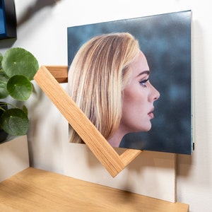 K&ouml;nnte beinhalten: Ein Holz-Plattenregal mit einer Schallplatte, auf der eine Frau mit blonden Haaren zu sehen ist. Die Platte tr&auml;gt den Titel "30" und die Frau schaut zur Seite.
