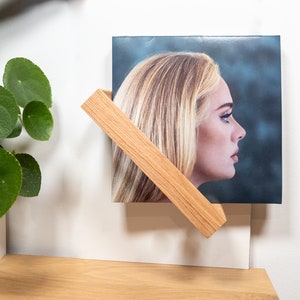 K&ouml;nnte beinhalten: Ein Holzst&auml;nder f&uuml;r Schallplatten mit einer Schallplatte, die eine Frau mit blonden Haaren zeigt. Die Schallplatte tr&auml;gt den Titel "25" und zeigt ein Foto von Adele.