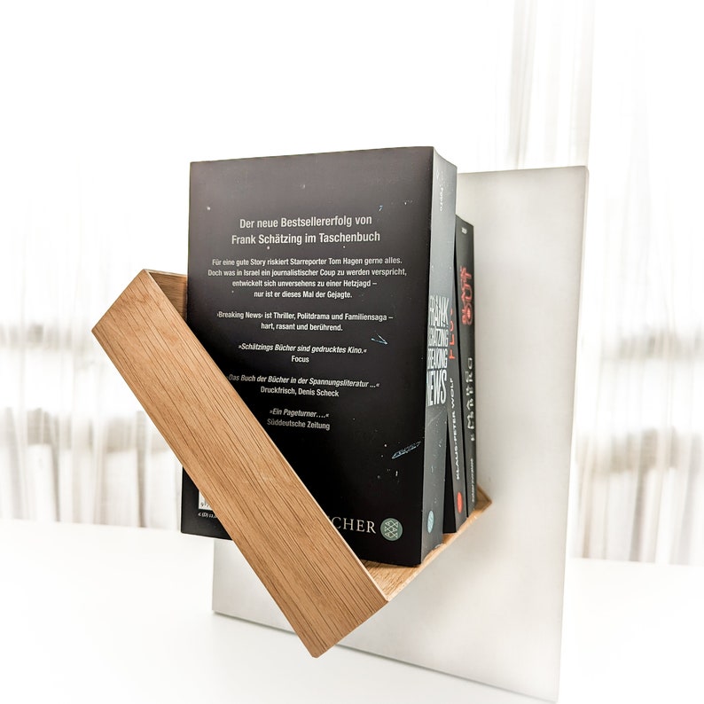 K&ouml;nnte beinhalten: Ein schwarz-wei&szlig;es Buch mit dem Titel "Breaking News" von Frank Sch&auml;tzing. Das Buch befindet sich auf einem Holzregal mit wei&szlig;em Hintergrund.
