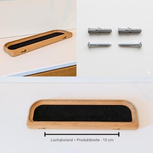 Op de afbeelding: Een houten plank met een zwart viltinzetstuk, getoond met schroeven en pluggen. De plank heeft een gebogen ontwerp en is gemaakt van lichtgekleurd hout. De tekst op de afbeelding luidt "Lochabstand = Produktbreite - 10 cm."