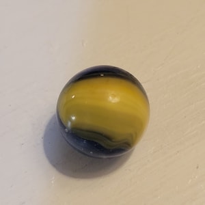 May include: A yellow and black glass marble with swirling patterns.
