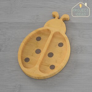 Op de afbeelding: Een houten bord in de vorm van een lieveheersbeestje met zwarte stippen. Het bord is gemaakt van bamboe en is perfect om snacks of maaltijden voor kinderen op te dienen.