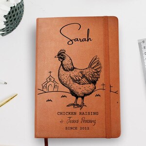 May include: A brown leather journal with the name "Sarah" in script. A detailed illustration of a chicken is featured, along with the text "Chicken Raising & Jesus Praising Since 2012". A ruler is visible.