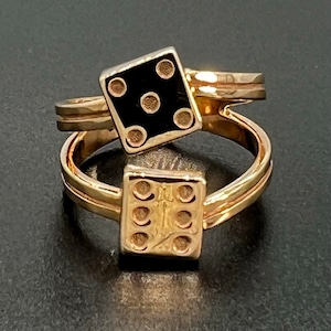 May include: A gold ring with two dice charms. One die is black with white dots and the other is gold with black dots.