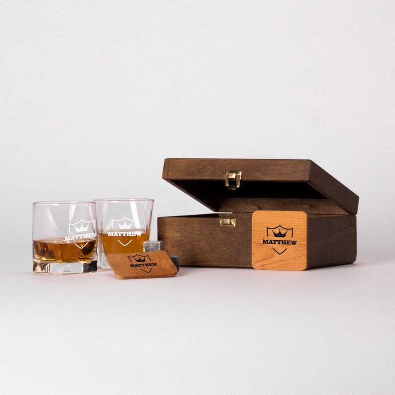 May include: A wooden box with a hinged lid, containing two personalized whiskey glasses and a set of whiskey stones. The box and glasses are engraved with the name "Matthew".