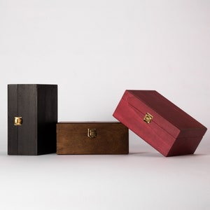 May include: Three wooden boxes with gold latches. The boxes are stacked on top of each other. The top box is red, the middle box is brown, and the bottom box is black.