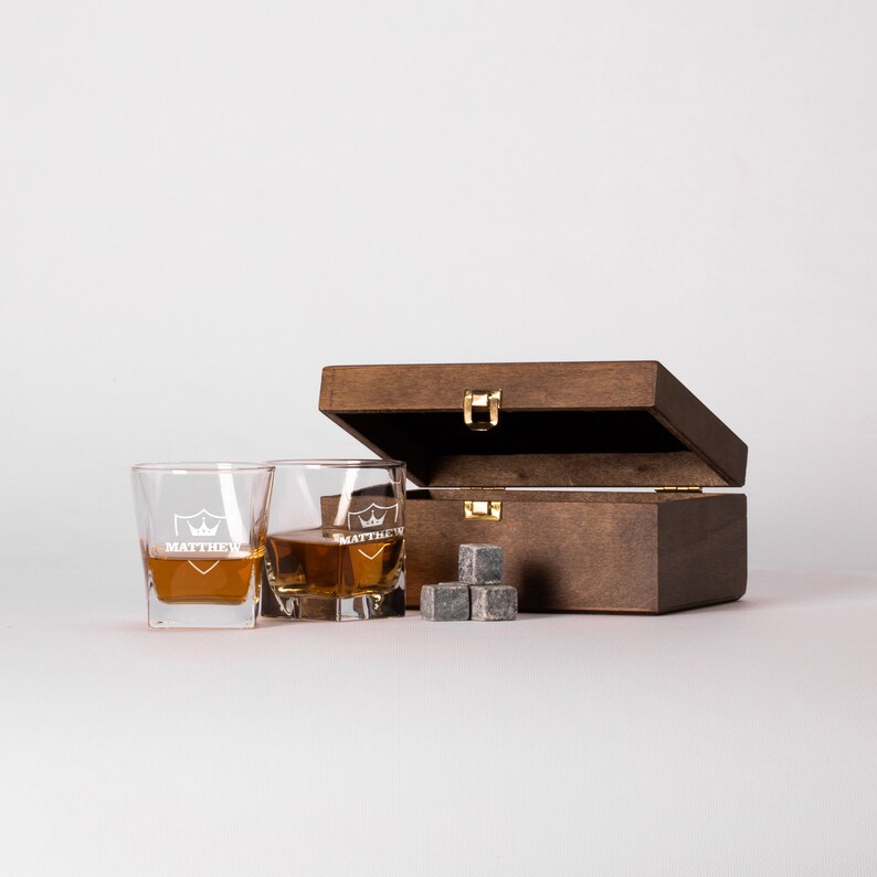 May include: Two clear glass whiskey glasses with the name "MATTHEW" etched on them, a wooden box with a gold latch, and four gray whiskey stones.