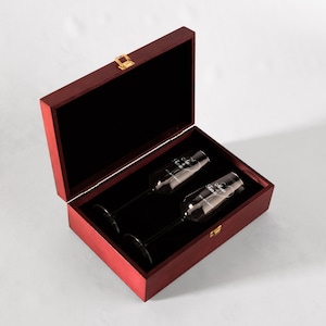 May include: A red wooden box with a gold latch, containing two clear champagne flutes with the words "Mr. & Mrs." etched on them.