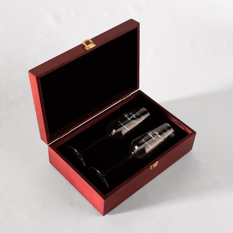 May include: A red wooden box with a gold latch, containing two clear champagne flutes with the words "Mr. & Mrs." etched on them.